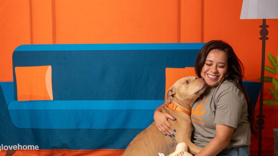 Sarah Shaw sitting on the ground with Peaches the dog in front of a backdrop of a couch and lamp